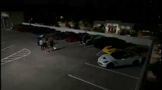 An aerial nighttime view of an HTX Corvettes meet, row of parked Corvettes (yellow, red, white) with members standing nearby. An aerial nighttime view of an HTX Corvettes meet, row of parked Corvettes (yellow, red, white) with members standing nearby.