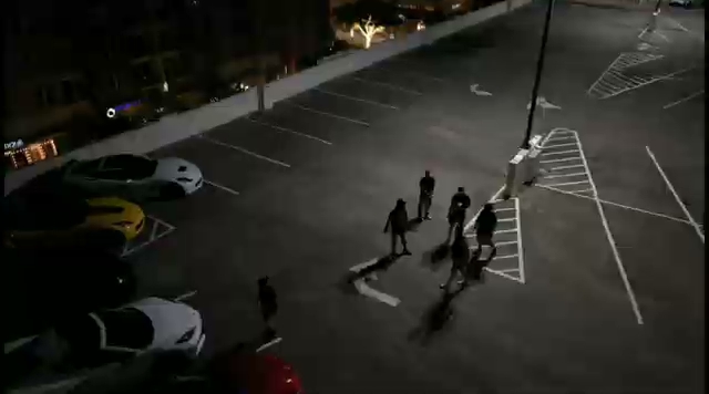 A nighttime parking lot with a yellow Corvette and a small group of members walking together between cars. A nighttime parking lot with a yellow Corvette and a small group of members walking together between cars.