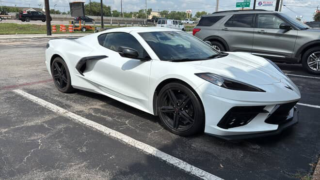 A white C8 Corvette with black wheels parked in a daytime lot. A white C8 Corvette with black wheels parked in a daytime lot.