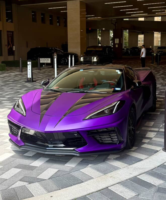 A purple-wrapped C8 Corvette with a black hood stripe, parked in a valet area. A purple-wrapped C8 Corvette with a black hood stripe, parked in a valet area.